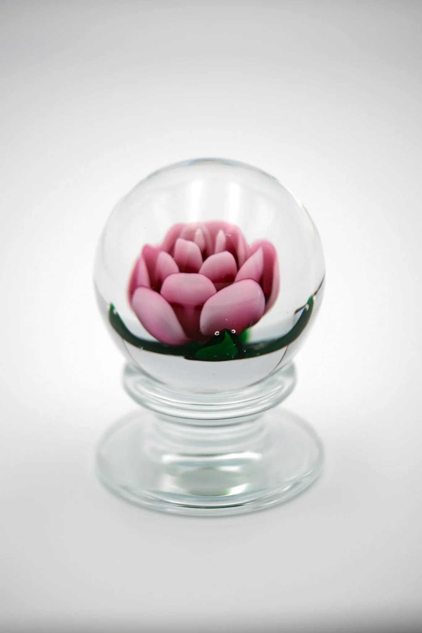 A small glass paperweight with a pink rose inside the globe sits atop a gray background