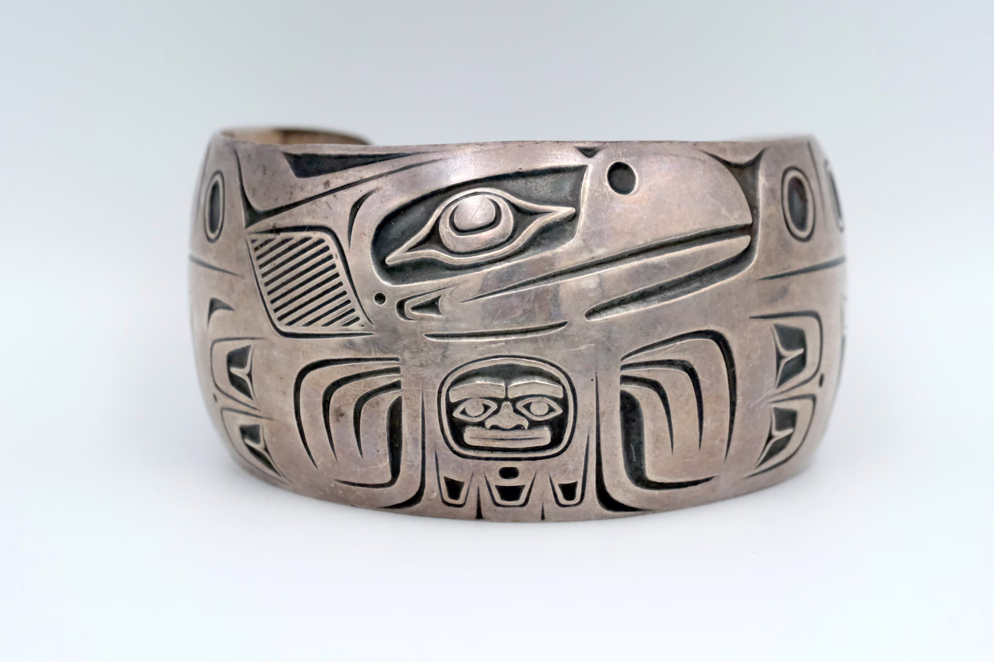 A silver bracelet with an indigenous pacific northwest pattern embellishing it.