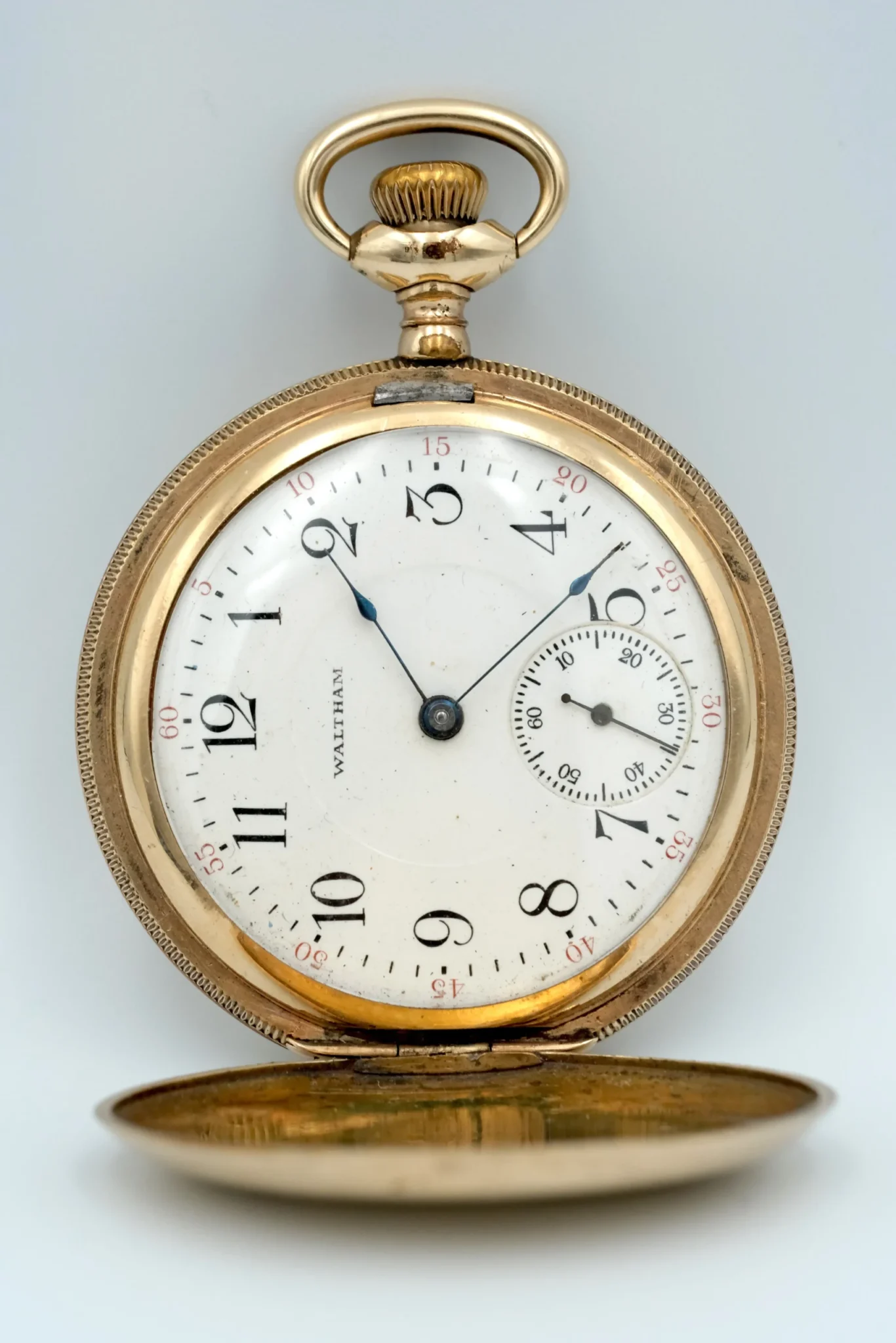 A Waltham Hunter case pocket watch with white dial and black arms in front of a gray background