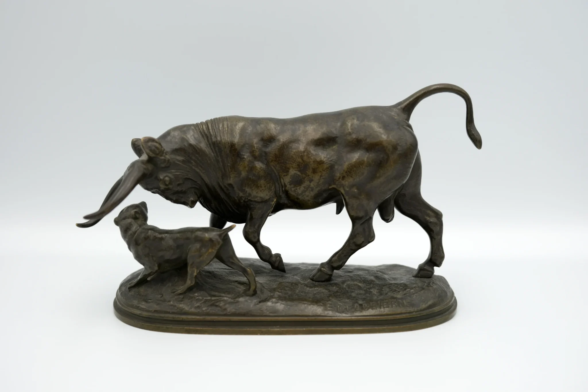 A bronze statue of a bull playing with a dog set in front of a gray background