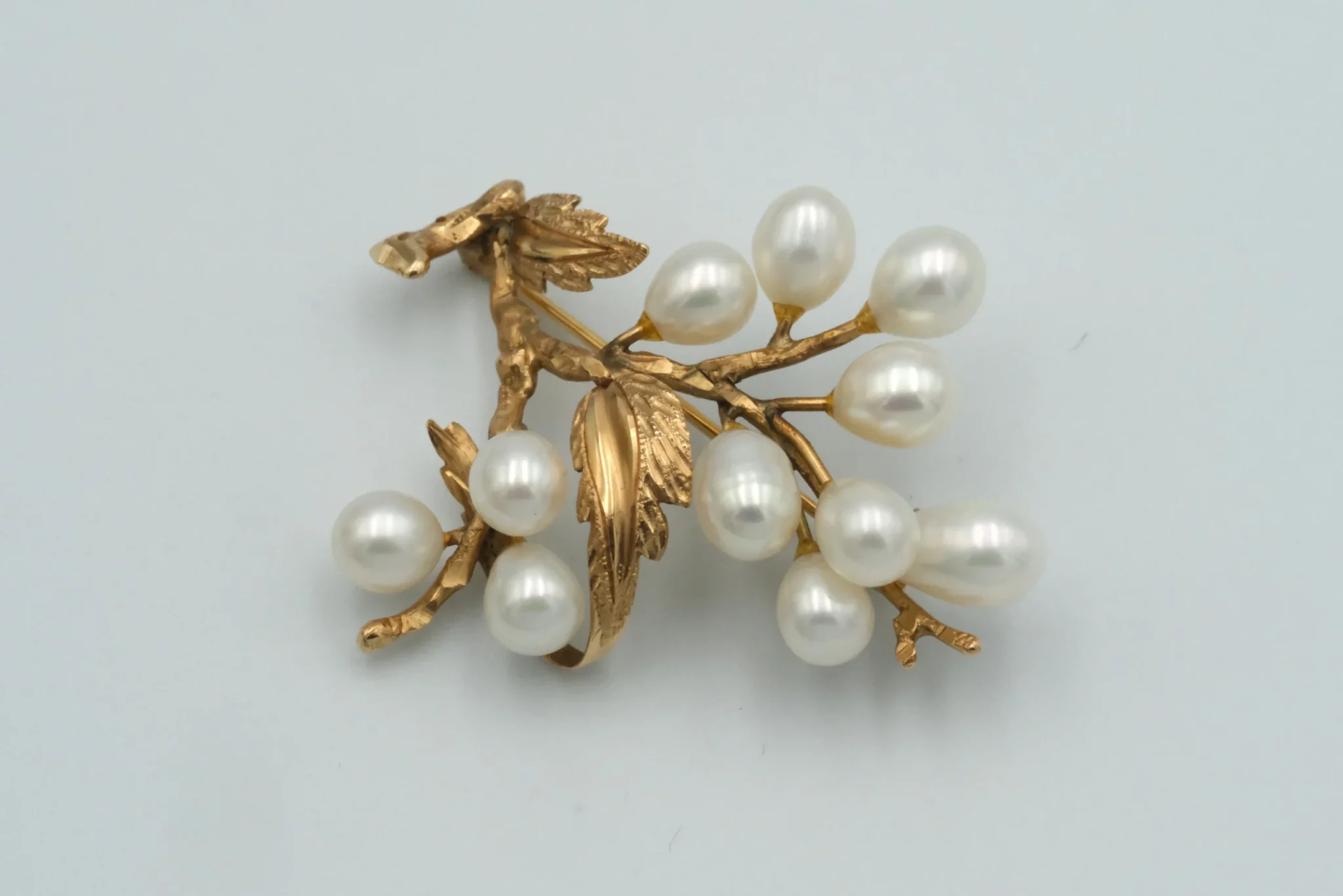A golden branch brooch with cultured pearls in front of a gray background