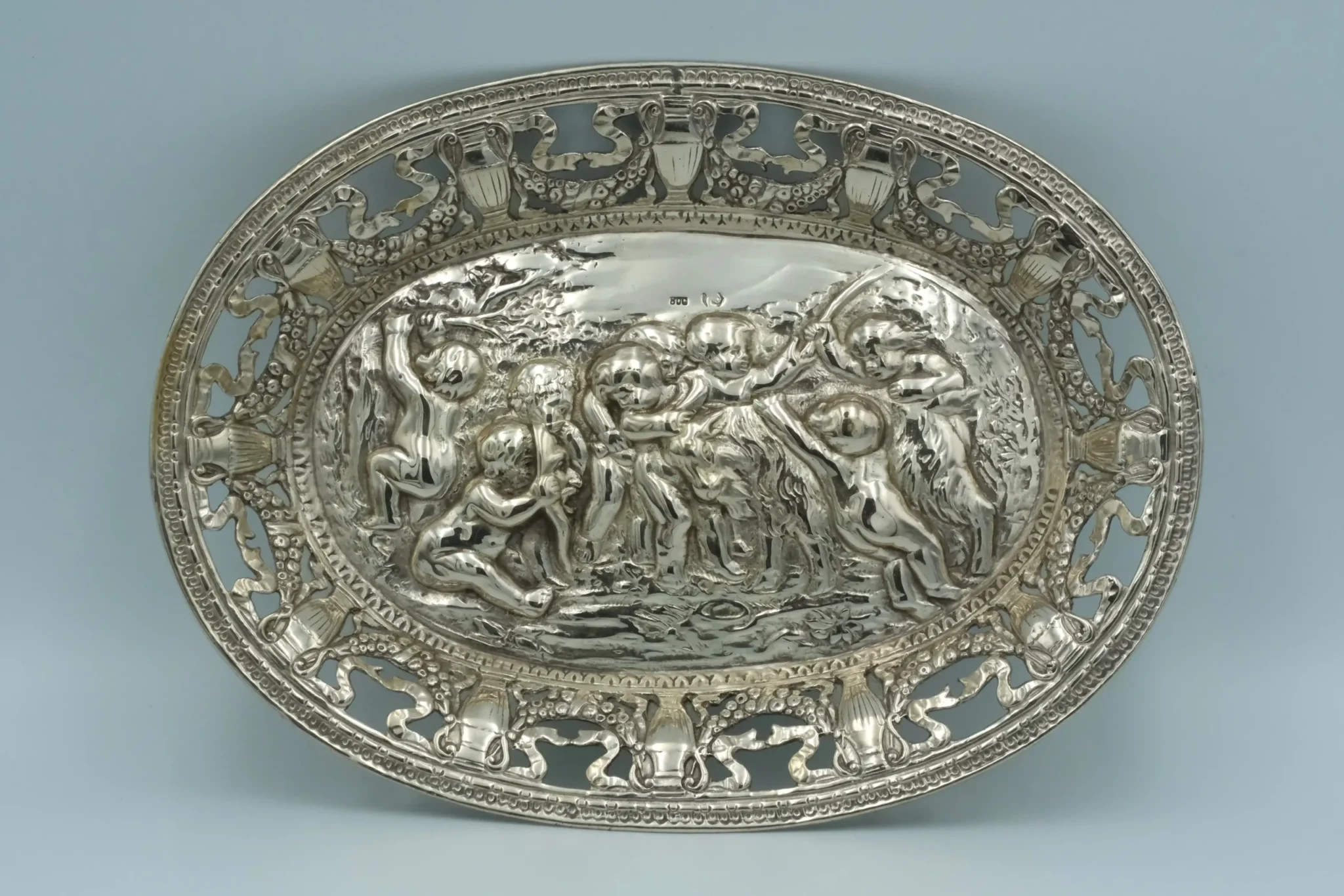 A German silver oval bonbon tray with a repousse cherup scene pierced border sitting atop a gray background