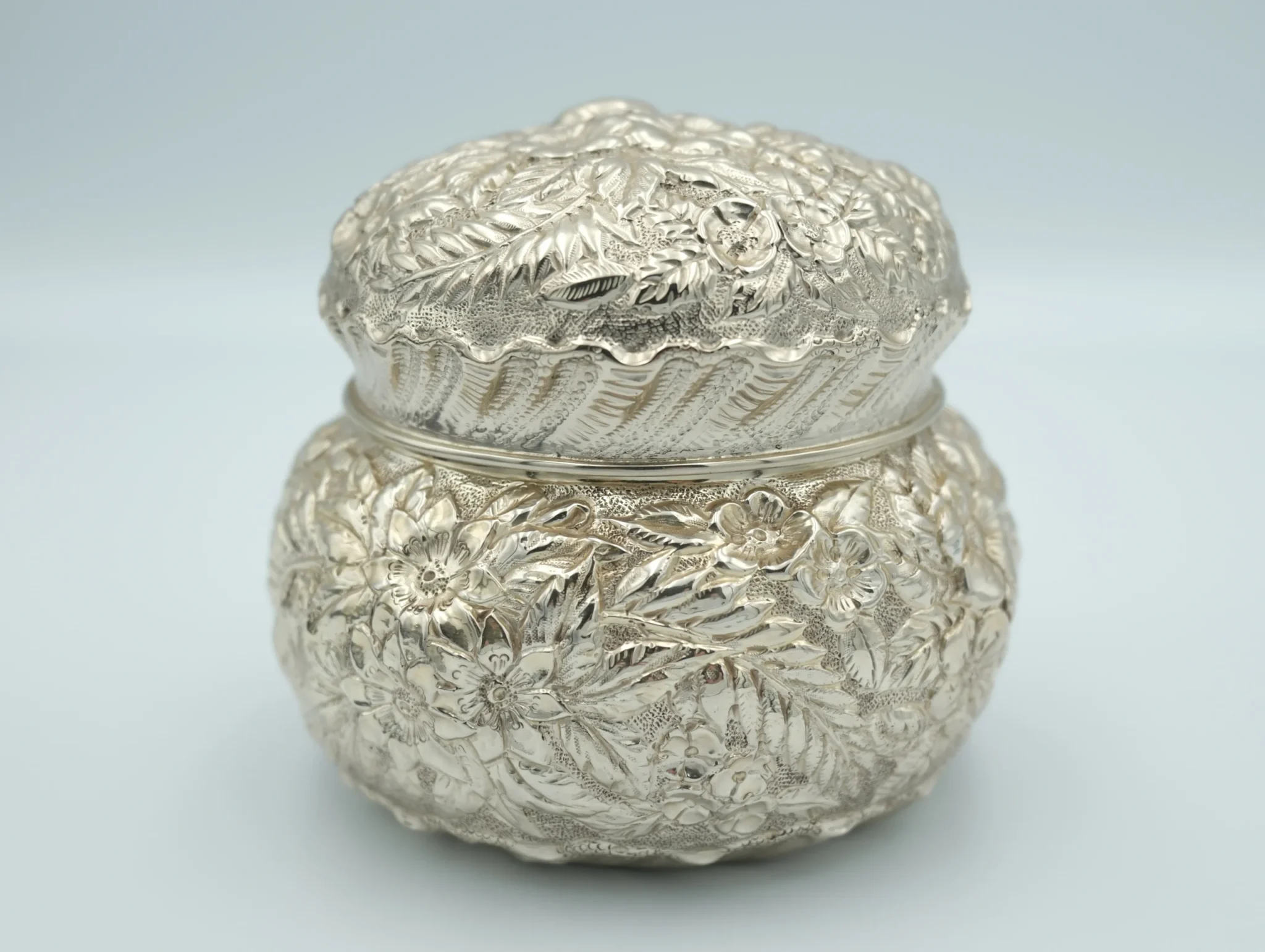 A silver repousse with textured sterling silver sits in front of a gray background