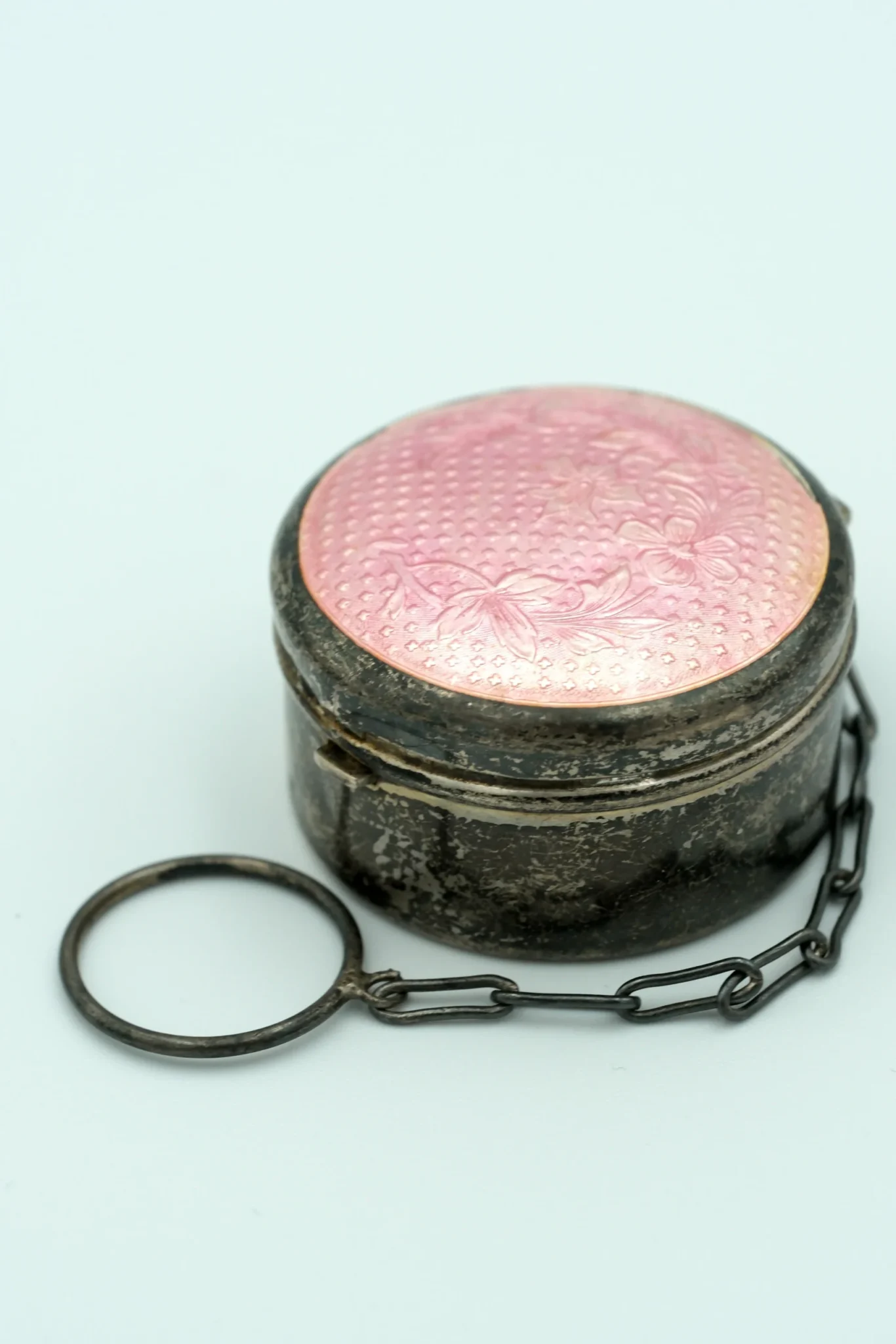 A chatelaine makeup compact, with a pink top and guilloche pink enamel in front of a gray background