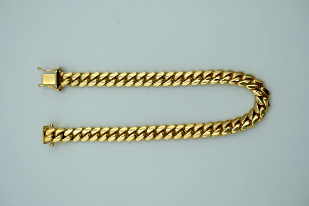 A gold cuban link bracelet sits atop a gray background