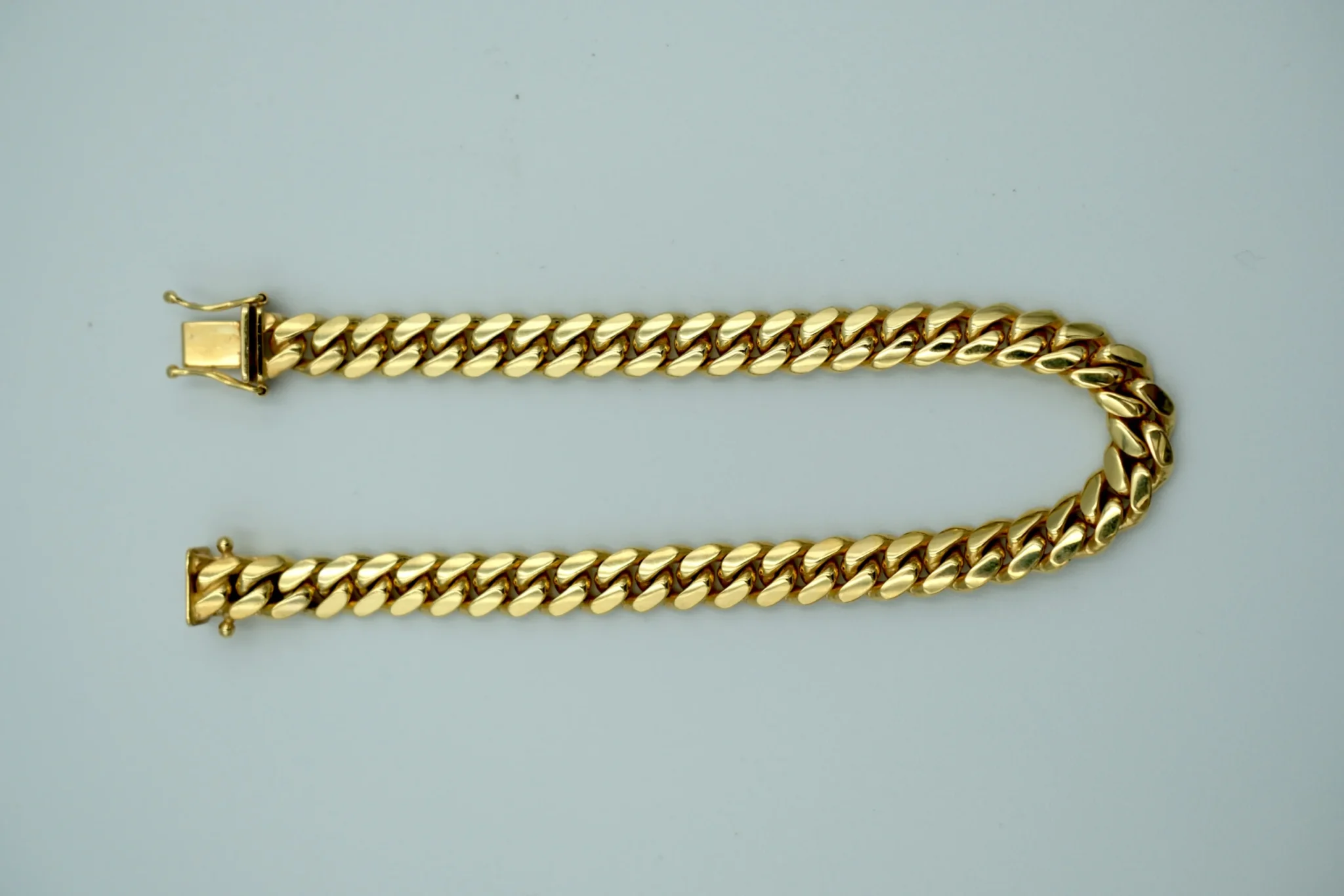 A gold cuban link bracelet sits atop a gray background