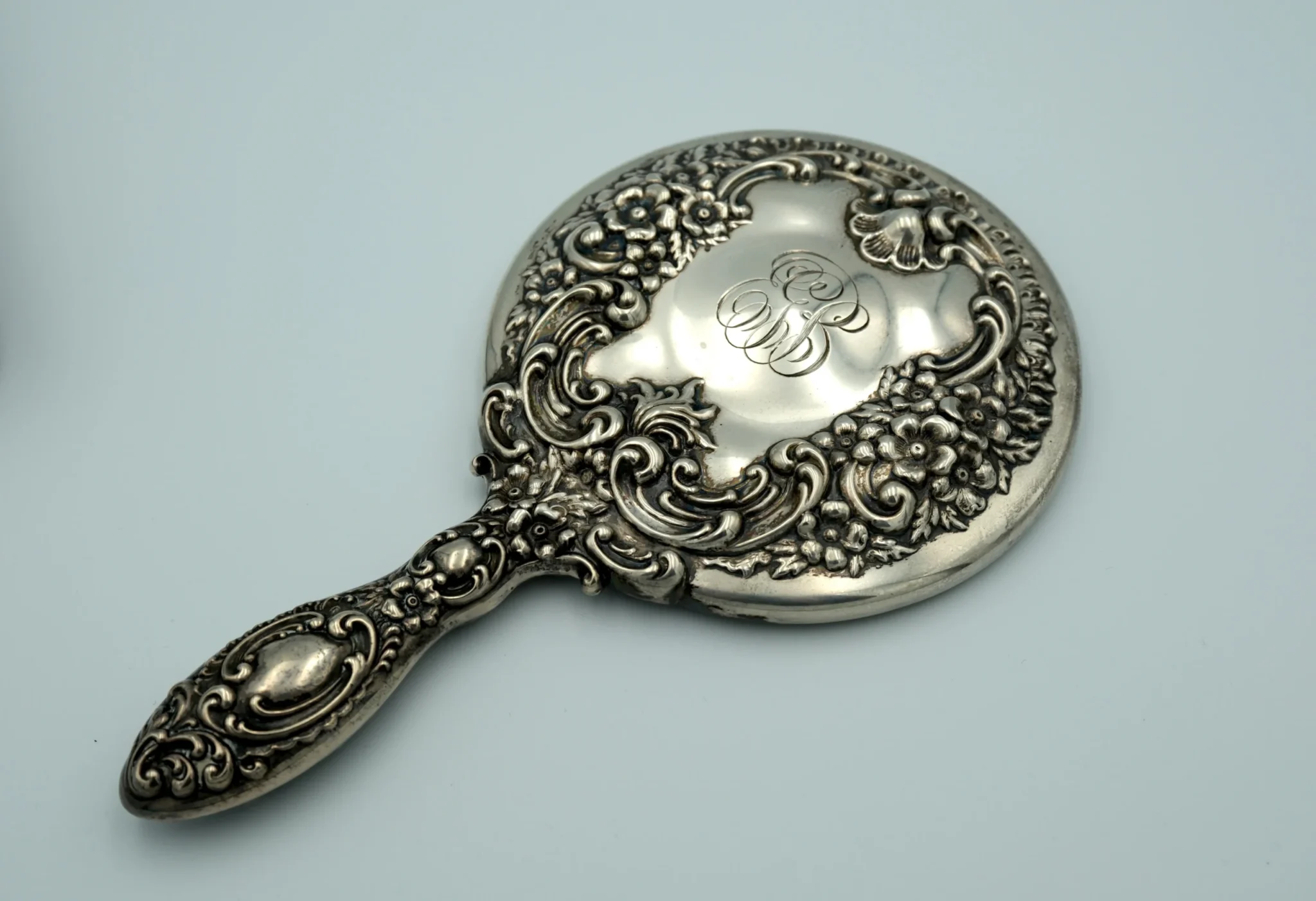 A sterling silver repousse hand mirror sitting face down atop a gray background