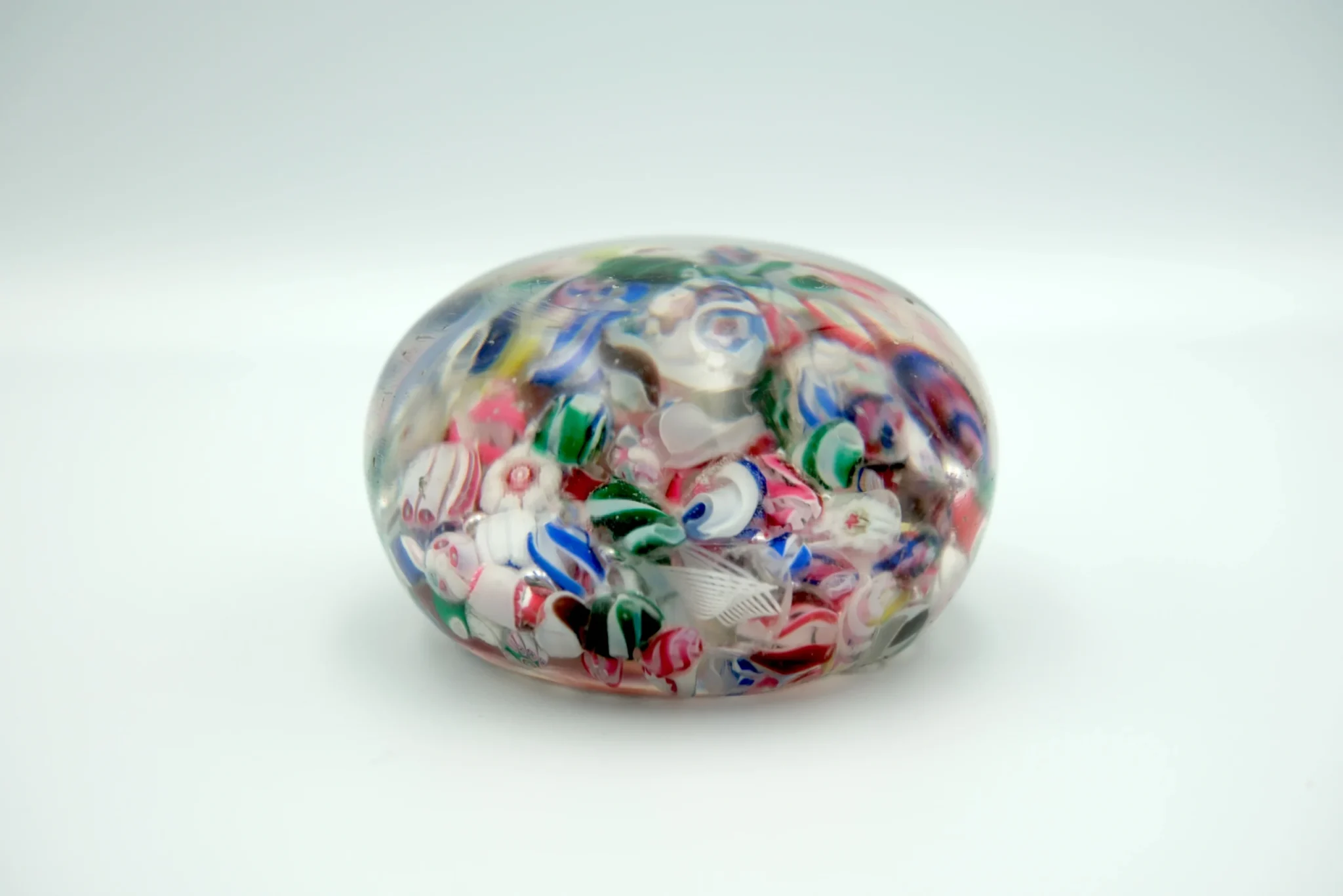 A multicolored Italian paperweight, with many different colors of glass inside, sitting atop a gray background