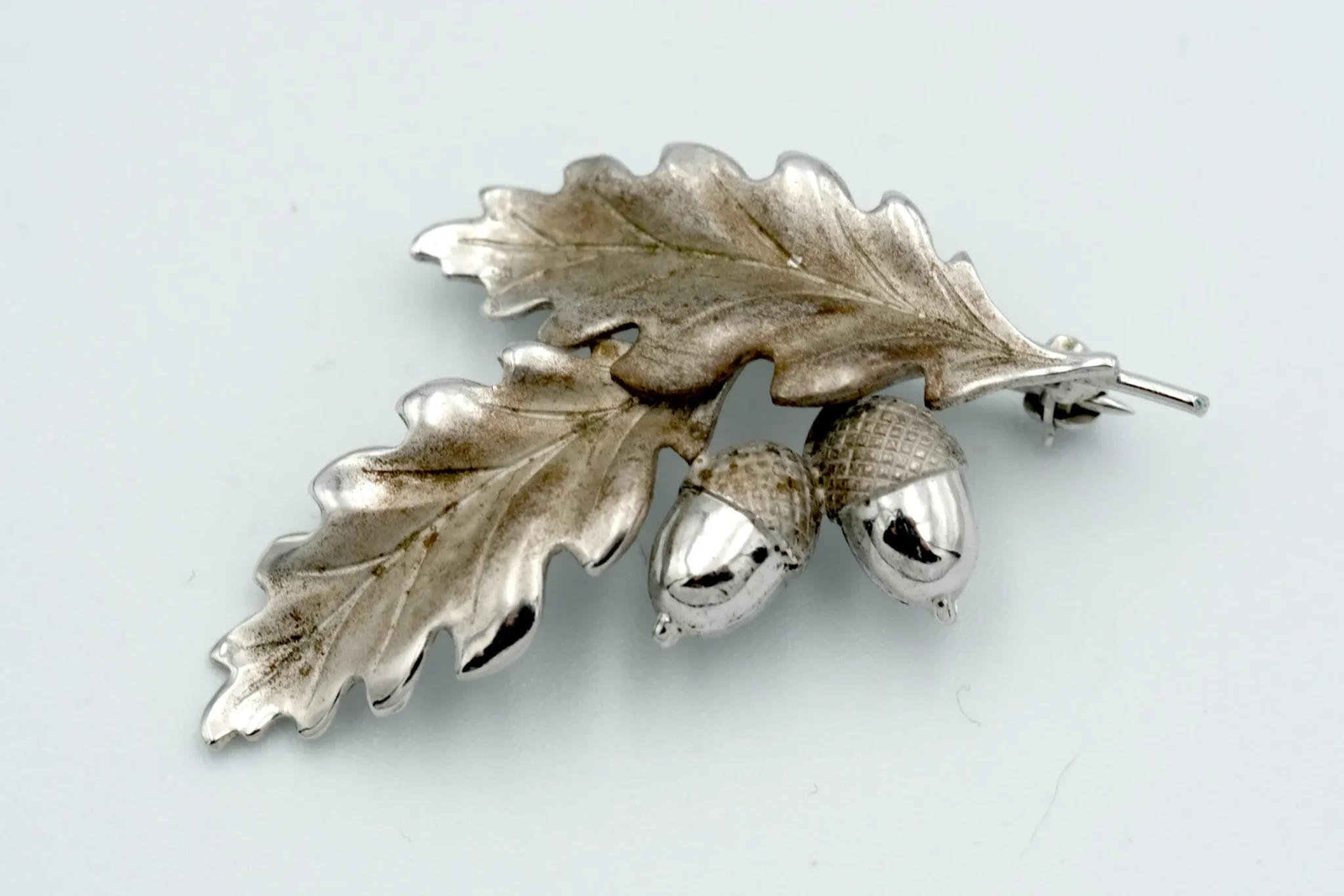 A sterling silver oak leaf and acorn brooch sitting atop a gray background