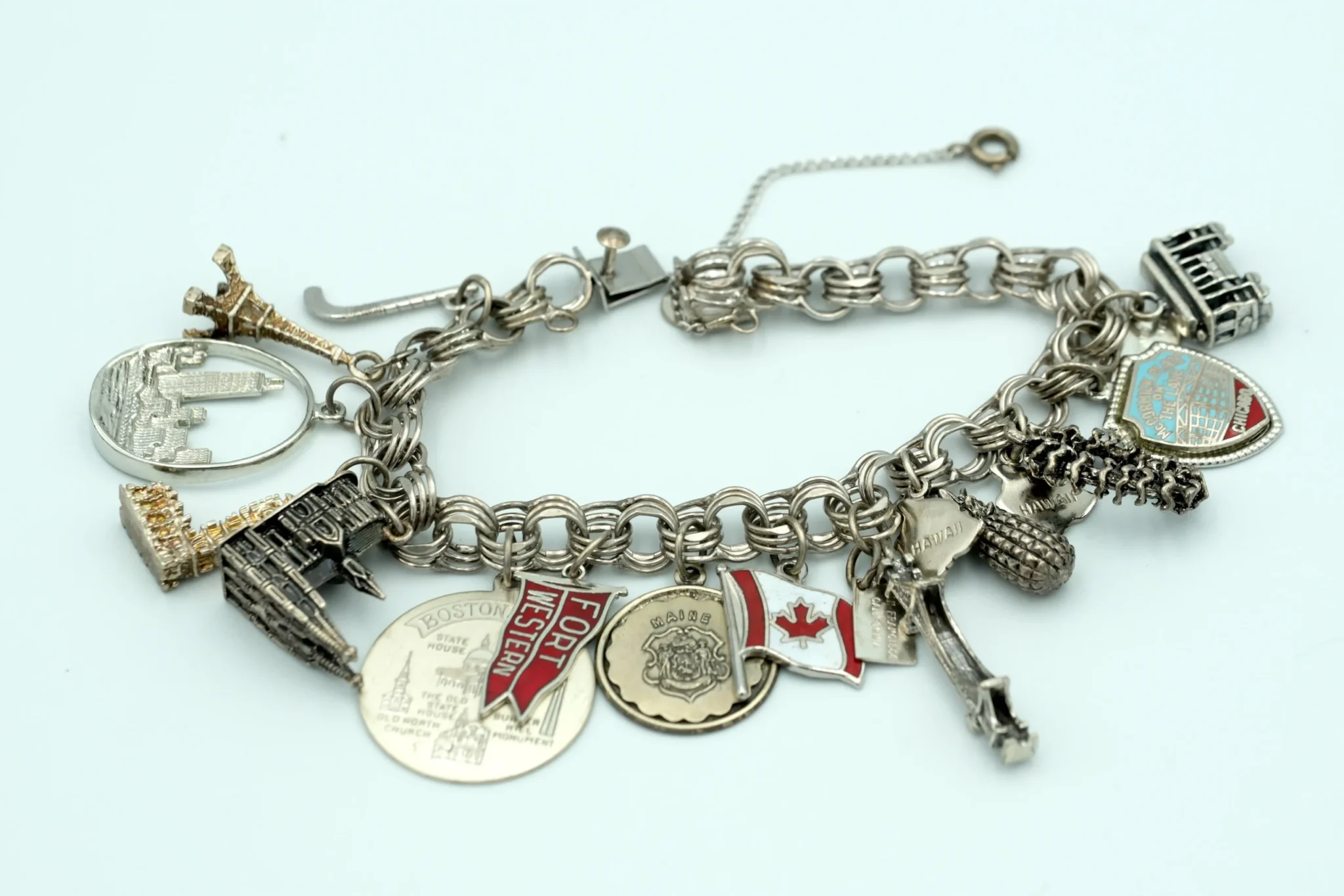 A silver bracelet with many different charms in sterling silver, in front of a gray background
