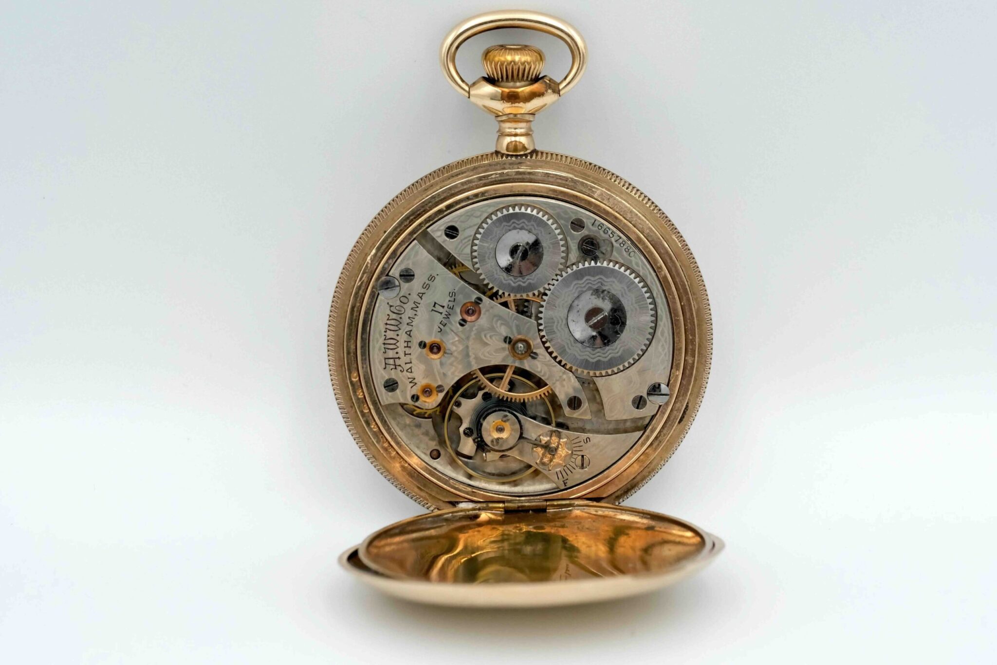Waltham hunter case pocket watch, image showing the movement of the pocket watch behind the white dial, in front of a gray background